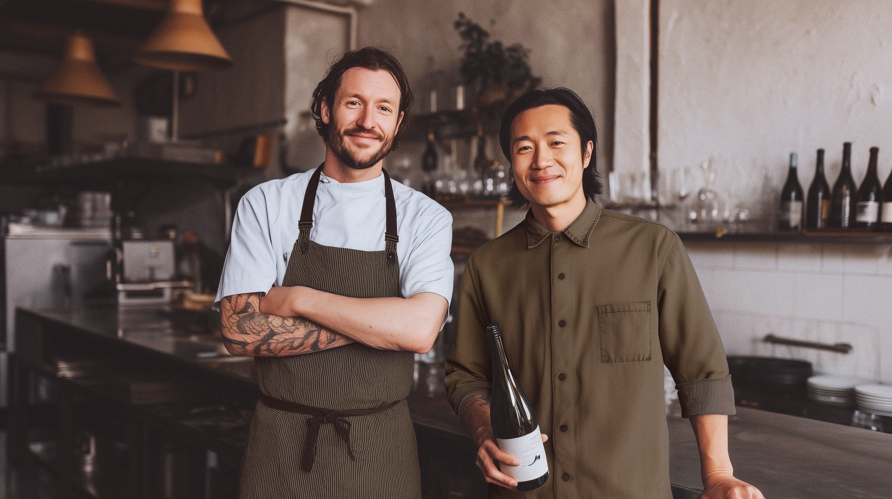 Two men standing in a kitchen, one holding a bottle of wine.